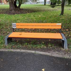 Pomarańczowa ławka w parku przy ul. Pogodnej w Swarzędzu; z boku tabliczka z numerami telefonów pomocowych.