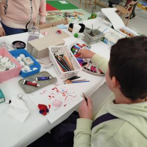 Stół plastyczny. Dziecko maluje gipsowe figurki; na blacie farby, pędzle, foremki i kartka z śladami farby.