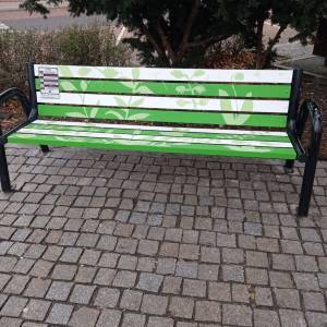 Ławka pomalowana w zielone liściaste wzory na białych i zielonych deskach, ustawiona na brukowanej nawierzchni
