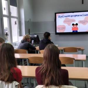 Grupa uczniów siedzi w klasie i słucha prowadzącej; na ekranie wyświetlony jest slajd ‘Bądź swoim sprzymierzeńcem