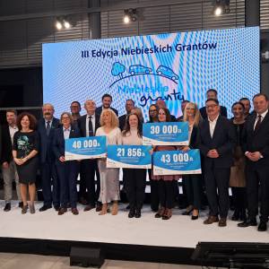 Laureaci i organizatorzy projektu podczas wręczenia grantów — kilka osób trzymających czeki, scena z bannerem Niebieskie Granty w tle.