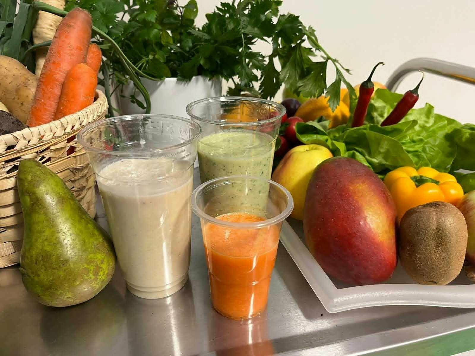 Świeże owoce i warzywa oraz przygotowane soki w plastikowych kubkach na stole podczas warsztatów dietetycznych dla seniorów