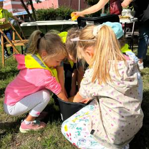 Zdjęcie przedstawia troje przedszkolaków myjących owoce w wiadrze z wodą.